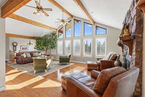 Living area with high vaulted ceiling, wood-type flooring, beam ceiling, a fireplace, and ceiling fan