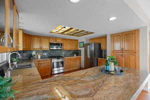 Kitchen featuring brown cabinetry, light wood-type flooring, stainless steel appliances, backsplash, and a textured ceiling