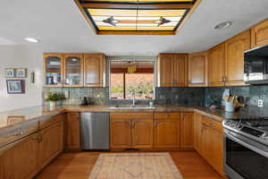 Kitchen featuring appliances with stainless steel finishes, brown cabinets, light wood-type flooring, glass insert cabinets, and recessed lighting