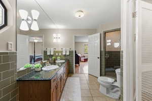 Ensuite bathroom with tile walls, light tile patterned floors, double vanity, a shower stall, and a wainscoted wall