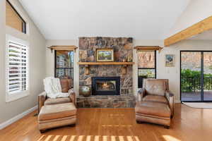 Living room with wood finished floors, a stone fireplace, and high vaulted ceiling