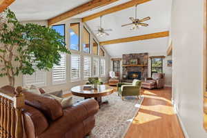 Living area with wood-type flooring, a fireplace, beam ceiling, high vaulted ceiling, and ceiling fan