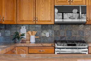 Kitchen featuring brown cabinetry, tasteful backsplash, appliances with stainless steel finishes, and dark stone counters