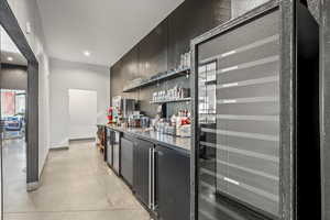 Indoor dry bar featuring dark cabinetry, beverage cooler, open shelves, recessed lighting, and fridge