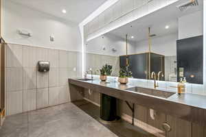 Bathroom featuring double vanity, concrete flooring, recessed lighting, a wainscoted wall, and tile walls