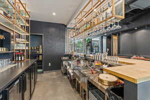 Indoor dry bar with beverage cooler, dark cabinetry, open shelves, recessed lighting, and wood counters