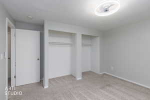 Unfurnished bedroom featuring light carpet, multiple closets, and a textured ceiling