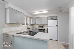 Kitchen with gray cabinetry, stainless steel appliances, light countertops, light tile patterned floors, and decorative backsplash