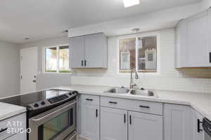 Kitchen featuring stainless steel range with electric cooktop, light countertops, backsplash, gray cabinetry, and a peninsula