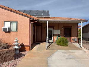 View of exterior entry featuring a tile roof, stucco siding, solar panels, and cooling unit