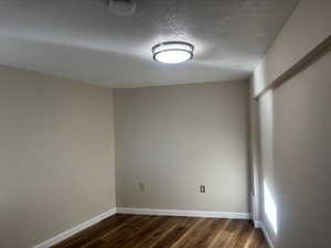 Empty room featuring a textured ceiling and dark wood-type flooring
