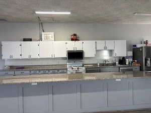 Kitchen with white cabinetry, appliances with stainless steel finishes, light stone countertops, and a textured ceiling