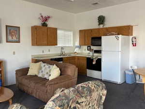 Kitchen with white appliances, light countertops, brown cabinetry, open floor plan, and dark carpet