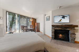 Carpeted bedroom with floor to ceiling windows, a stone fireplace, a chandelier, and access to outside