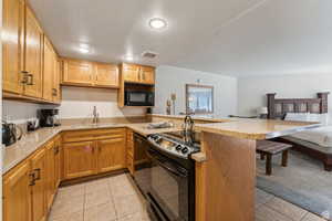 Kitchen with black appliances, light tile patterned floors, a peninsula, light stone counters, and recessed lighting