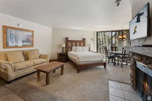 Bedroom with a stone fireplace, a chandelier, a wall of windows, light tile patterned flooring, and light carpet