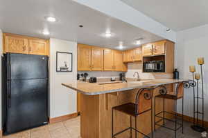 Kitchen with a kitchen bar, black appliances, light tile patterned floors, a peninsula, and light stone countertops
