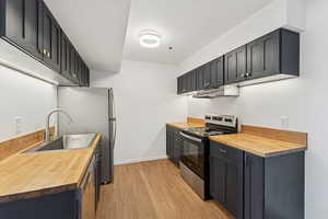 Kitchen featuring butcher block countertops, stainless steel appliances, dark cabinets, and light wood-style floors