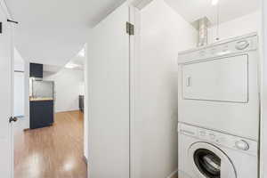 Washroom with stacked washer / drying machine and light wood-style floors