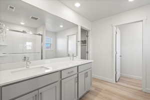 Full bath with light wood-style floors, a stall shower, double vanity, and recessed lighting