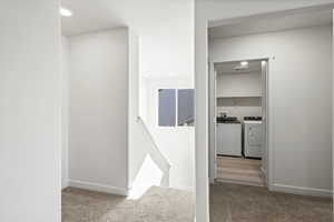 Hallway with an upstairs landing, light carpet, washer and clothes dryer, and recessed lighting