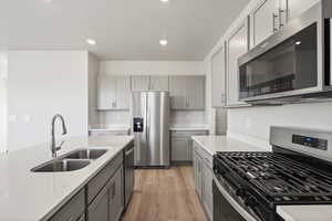 Kitchen featuring appliances with stainless steel finishes, gray cabinetry, light wood-style flooring, recessed lighting, and light stone counters
