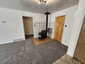 Unfurnished room featuring a wood stove, heating unit, carpet, and tile walls