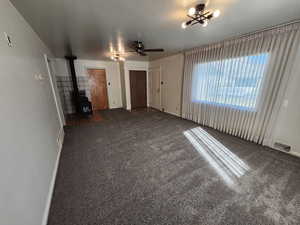Unfurnished living room featuring a wood stove, carpet flooring, a ceiling fan, and a chandelier