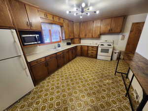 Kitchen featuring white appliances, light countertops, a chandelier, and brown cabinetry
