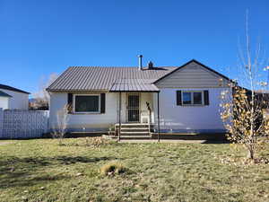 View of front facade with a front lawn, a metal roof, and a porch