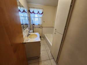 Bathroom featuring vanity, light tile patterned flooring, a garden tub, tile walls, and a wainscoted wall
