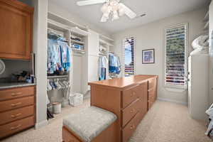 Walk in closet with light carpet and a ceiling fan