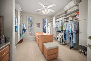 Walk in closet with light colored carpet and a ceiling fan