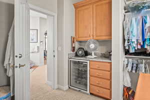 Bar area with wine cooler, light carpet, brown cabinetry, and light stone countertops