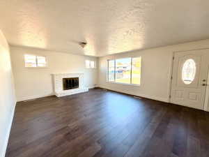 Unfurnished living room featuring a brick fireplace, healthy amount of natural light, dark wood-type flooring, and a textured ceiling
