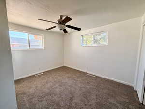 Unfurnished room featuring dark carpet, a textured ceiling, and a ceiling fan