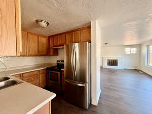 Kitchen featuring appliances with stainless steel finishes, light countertops, a textured ceiling, dark wood-type flooring, and a brick fireplace