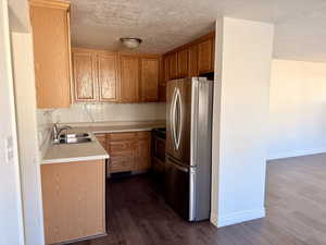 Kitchen featuring light countertops, appliances with stainless steel finishes, dark wood-style flooring, a textured ceiling, and brown cabinetry