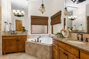 Full bathroom featuring two vanities, backsplash, hanging lights, and a bath