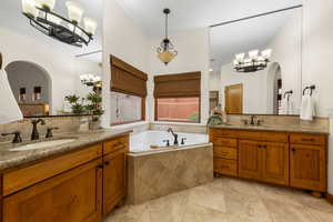 Bathroom with a chandelier, two vanities, a garden tub, and decorative backsplash