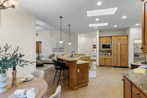 Kitchen with decorative light fixtures, wood finish cabinetry, built in appliances, a kitchen breakfast bar, and light stone countertops