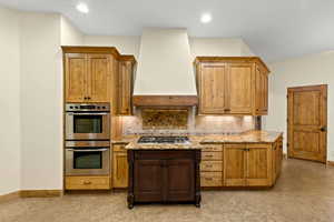 Kitchen with backsplash, custom exhaust hood, appliances with stainless steel finishes, light stone counters, and recessed lighting