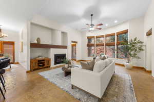 Living area featuring a glass covered fireplace, a ceiling fan, suspended lighting, and concrete floors