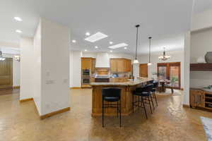 Kitchen featuring suspended lighting, light stone counters, wood finish cabinets, a skylight, and a kitchen breakfast bar