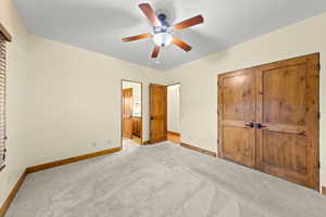 Unfurnished bedroom with light carpet, a ceiling fan, a closet, and ensuite bathroom