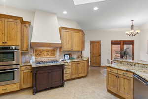 Kitchen with stainless steel appliances, suspended lighting, light stone countertops, light floors, and decorative backsplash