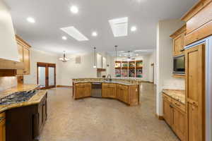 Kitchen with a chandelier, light stone countertops, a skylight, built in appliances, and ventilation hood