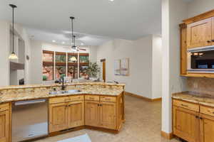 Kitchen featuring light stone counters, dishwasher, a ceiling fan, and wood finish cabinetry