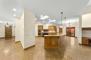 Kitchen featuring a chandelier, brown cabinetry, pendant lighting, a skylight, and light stone counters