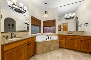 Bathroom featuring a chandelier, two vanities, a bath, and backsplash